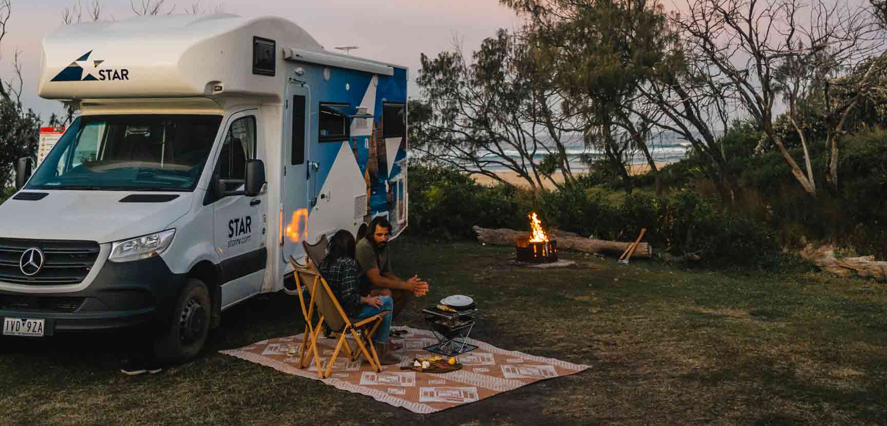 Couple eating outside motorhome on picnic blanket